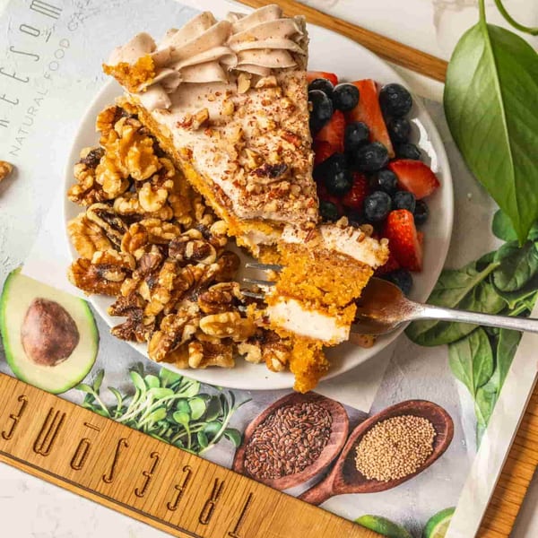 A slice of healthy carrot cake with walnuts, berries, and a fork taking a bite.