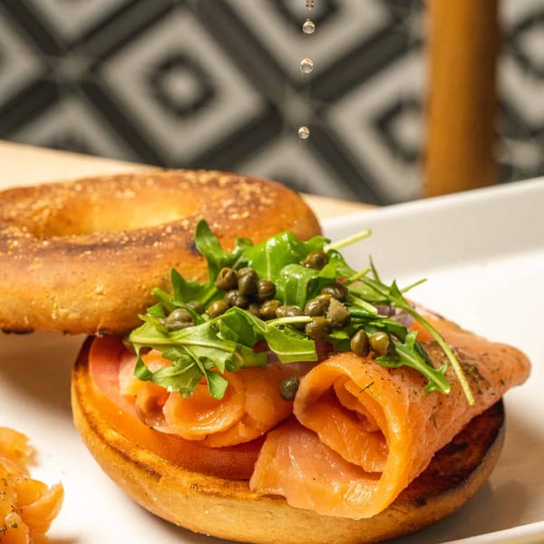 A bagel with smoked salmon, arugula, and capers, with oil drops falling onto it.